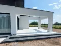 Nowe, białe płytki tarasowe lśnią na tle nowoczesnej architektury. Trwają prace nad układaniem płyt tarasowych, tworząc elegancką przestrzeń.