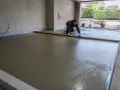Pracownik wyrównuje świeżą wylewkę pod taras na gruncie, przygotowując solidną podstawę.