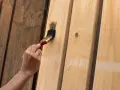 Ręka maluje pędzlem jasne panele ścienne MDF ciemną farbą, nadając im nowy wygląd.