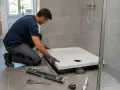 Instalator montuje brodzik wysoki, używając poziomicy i klucza. Narzędzia i silikon leżą obok.