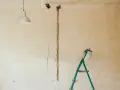 Pękające ściany starego domu, widoczna instalacja elektryczna i drabina.