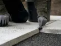 Ręce w rękawiczkach nakładają fugę do płyt tarasowych, tworząc trwałe i estetyczne połączenie.