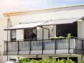 Nowoczesny balkon z balustradą i markizami. Szklana ścianka to pomysł, jak odgrodzić balkon, zapewniając prywatność i styl.