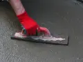 Ręka w czerwonej rękawicy wygładza świeżą wylewkę do garażu za pomocą kielni.