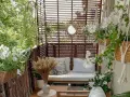 Przytulny balkon z drewnianą sofą, białymi kwiatami i ozdobnym lustrem w kształcie słońca.