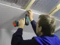 Mężczyzna wykonuje montaż paneli PCV na suficie, używając wkrętarki.