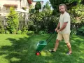 Mężczyzna z dredami pokazuje, jak ustawić siewnik do trawy, rozsypując nawóz na trawniku.