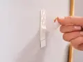Dłoń odrywa taśmę z napisem "Powerstrips", pokazując alternatywę dla gwoździ do ściany.