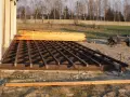 Drewniana konstrukcja tarasu w trakcie budowy, obok stos desek.