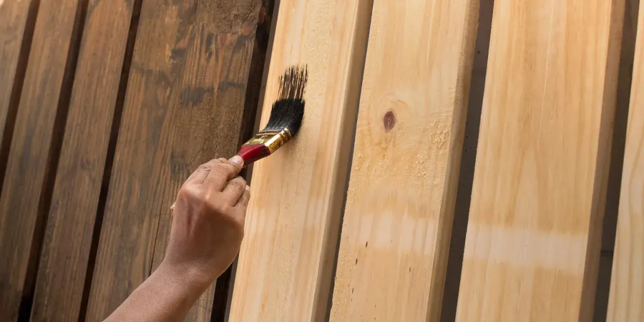Ręka maluje pędzlem jasne panele ścienne MDF ciemną farbą, nadając im nowy wygląd.