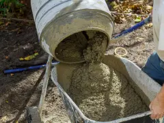 Mieszanie betonu w betoniarce, gotowego do użycia. Proces, jak zrobić beton, jest widoczny, gdy świeża masa spływa do taczki.