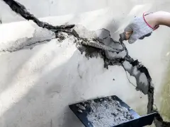 Ręka w rękawicy nakłada gips do dziur w ścianie, używając kielni. Naprawa pęknięć na betonie.