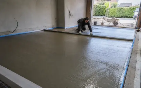 Pracownik wyrównuje świeżą wylewkę pod taras na gruncie, przygotowując solidną podstawę.