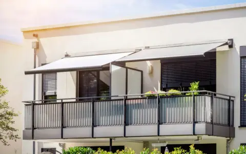 Nowoczesny balkon z balustradą i markizami. Szklana ścianka to pomysł, jak odgrodzić balkon, zapewniając prywatność i styl.