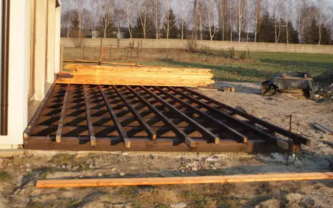 Drewniana konstrukcja tarasu w trakcie budowy, obok stos desek.