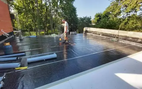 Pracownik wykonuje układanie płyt tarasowych na suchym betonie, używając palnika do obróbki papy.