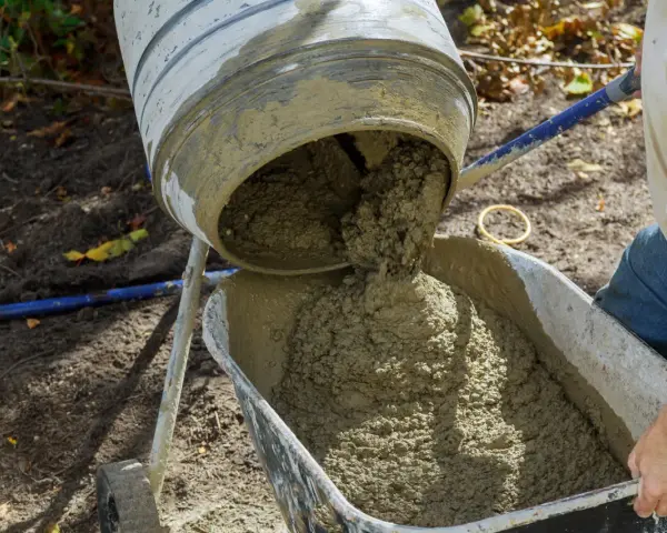 Mieszanie betonu w betoniarce, gotowego do użycia. Proces, jak zrobić beton, jest widoczny, gdy świeża masa spływa do taczki.
