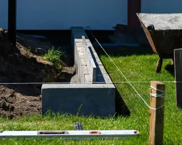 Budowa fundamentu pod ogrodzenie. Betonowe bloczki tworzą solidną podstawę, a niwelacyjna linka wyznacza precyzyjną linię.