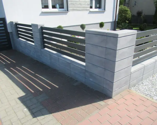 Nowoczesne ogrodzenie z betonowych słupków i ciemnoszarych paneli. Kolor ogrodzenia idealnie komponuje się z elewacją domu.