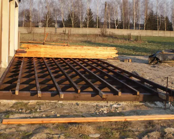 Drewniana konstrukcja tarasu w trakcie budowy, obok stos desek.