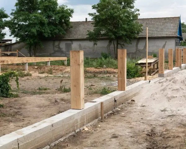 Rozpoczyna się montaż ogrodzenia. Widać betonowy fundament, drewniane słupki i budowę podłogi na podwyższeniu.