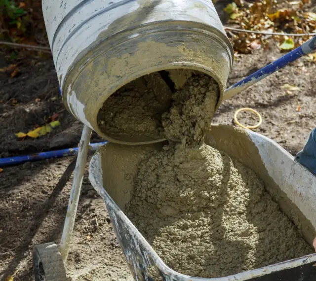 Mieszanie betonu w betoniarce, gotowego do użycia. Proces, jak zrobić beton, jest widoczny, gdy świeża masa spływa do taczki.