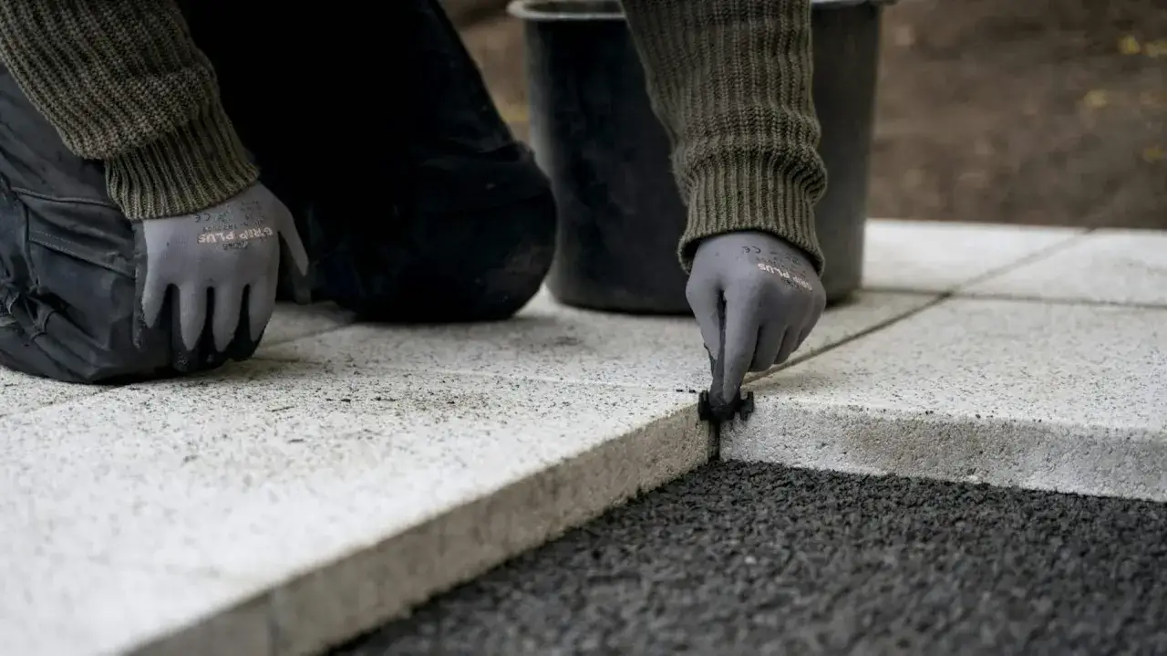 Ręce w rękawiczkach nakładają fugę do płyt tarasowych, tworząc solidne i estetyczne wykończenie.