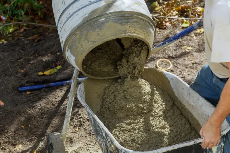 Mieszanie betonu w betoniarce, gotowego do użycia. Proces, jak zrobić beton, jest widoczny, gdy świeża masa spływa do taczki.